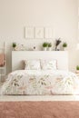 Pink carpet and posters in bright bedroom interior with plants above bed with cushions. Real photo Royalty Free Stock Photo