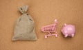 Pink ceramic piggy bank, miniature shopping cart and full canvas bag on brown background, top view Royalty Free Stock Photo