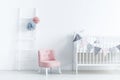 Pink chair next to white cradle in pastel baby`s bedroom interio Royalty Free Stock Photo