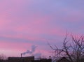 Pink clouds in the sky during sunset. Smoke from a chimney against a pink sky