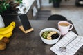 Pink coffee cup, chopped fruits in bowl and blueberries, spoon, phone in kitchen Royalty Free Stock Photo