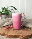 Pink coffee latte macchiato in a glass cup on a wooden backing decorated with dried flower