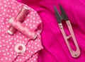 Pink colored flat lay top view sewing tools with thread and scissors on pink fabric background