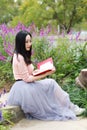 Happy Asian Chinese woman girl dream sit pray flower field autumn fall park lawn hope nature read book knowledge freedom carefree Royalty Free Stock Photo