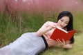 Happy Asian Chinese woman girl lying on grass dream pray flower field autumn fall park lawn hope nature read book knowledge Royalty Free Stock Photo