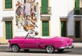 Pink convertible passing mural in Havana Cuba