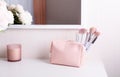 Pink cosmetic bag and makeup brushes on a white dressing table against the background of a mirror and a decorative candle. Royalty Free Stock Photo