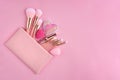 A pink cosmetics bag with make-up brushes and makeup products spilling out on to a pink background.