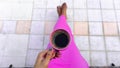 A pink cup of black coffee in a tan skin woman`s hand wearing fresh violet dresss, sitting on a wooden chair on grey tiles Royalty Free Stock Photo