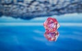 Pink D20 on blue reflecting surface 2