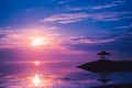 Pink dawn the sun and the gazebo at Sanur beach, Bali, Indonesia. A calm surface of sea water that reflects the sun and cloudy sky