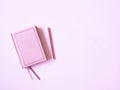 Pink diary with a pen on a pink background.