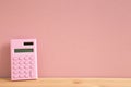 Pink digital calculator on wooden desk with pink background