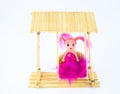 A pink doll sitting on a wooden swing made of toothpicks with an isolated white background Royalty Free Stock Photo