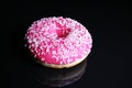Pink donut on black reflective studio background