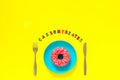 Carbohydrates and Pink donut on blue plate and knife fork on yellow background.