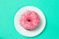 Pink donut with pink sprinkles on the white plate isolated.Pink dough on green background Royalty Free Stock Photo