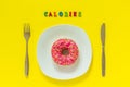 Calories and Pink donut on white plate and knife fork on yellow background. Royalty Free Stock Photo