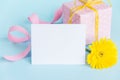 Pink dotted gift box, yellow gerbera flower and empty card over a blue background.