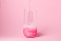 A pink drink is poured into a glass on a pink background. Carbonated sweet water. Royalty Free Stock Photo