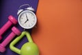 Pink dumbbell, alarm clock, kettle bell and purple yoga mat on orange table background Royalty Free Stock Photo