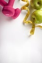 Pink dumbbells with apple and tape measure vertical composition