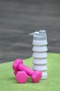 Pink dumbbells and silicone water bottle on yoga mat. Close up. Equipment for sports. Vertical frame