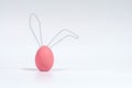 Pink Easter egg with ears made of wire. The concept of the Easter Bunny. White isolated background with soft shadow