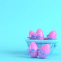 Pink easter eggs with bow in a wicker basket on bright blue background in pastel colors