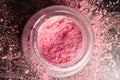 Pink eyeshadow in open jar on dark background