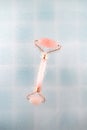 Pink face roller massager made from natural quartz stone over blue ÃÂeramic tile background with drops of water