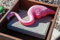 A pink flamingo ornament in a metal box