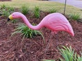 A pink flamingo yard ornament staked in a garden in front of a house