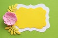 pink flower and shiny yellow leaves on a green paper background and two curly sheets of yellow and white paper.