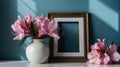 pink flowers in a vase next to a blank frame in a blue wall background Royalty Free Stock Photo