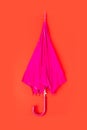 Pink folded umbrella on red background. Nobody