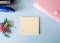 Pink folder, blue stapler, color clips and note paper on white table