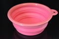 Pink folding and multifunctional rubber plate, a bowl with a plastic edging on a black glossy surface.