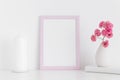 Pink frame mockup with pink roses in a vase and candle on a white table.Portrait orientation Royalty Free Stock Photo