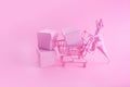 Pink Friday concept. Funny pink dinosaur toy with shopping cart full of present boxes on pink background