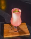 Pink fruit cocktail in a tall tulip glass served on a black wooden table in a restaurant