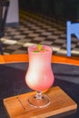 Pink fruit cocktail in a tall tulip glass served on a black wooden table in a restaurant