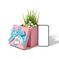 A pink gift box with easter eggs and grass inside, accompanied by a blank phone screen Royalty Free Stock Photo
