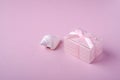 Pink gift box with ribbon near to white seashell on soft pink background