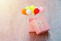 Pink gift box with silver ribbon and colorful balloon on wooden background. minimal hollyday concept