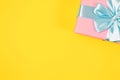 Pink gift box tied with blue ribbon with bow at the top on yellow background. Copy space for text. Minimal flat lay. Top view. Royalty Free Stock Photo