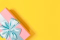 Pink gift box tied with blue ribbon with bow at the top on yellow background. Copy space for text. Minimal flat lay. Top view. Royalty Free Stock Photo