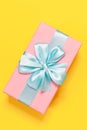 Pink gift box tied with blue ribbon with bow at the top on yellow background. Minimal flat lay. Top view. Royalty Free Stock Photo