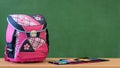 Pink girly school bag and pencil case on a desk against green board. First day of school. Royalty Free Stock Photo