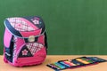 Pink girly school bag and pencil case on a desk against greenboard. First day of school.